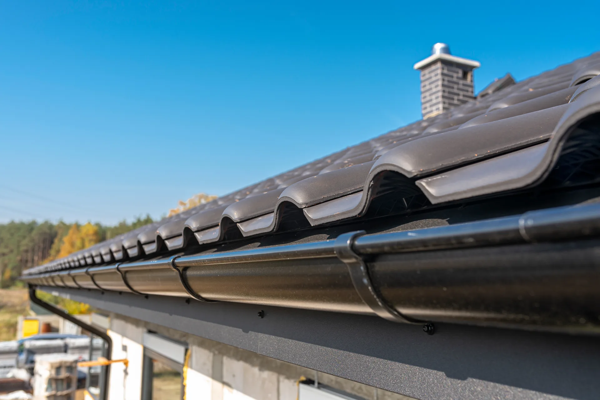 Black gutter running along the edge of a dark tiled roof with a chimney